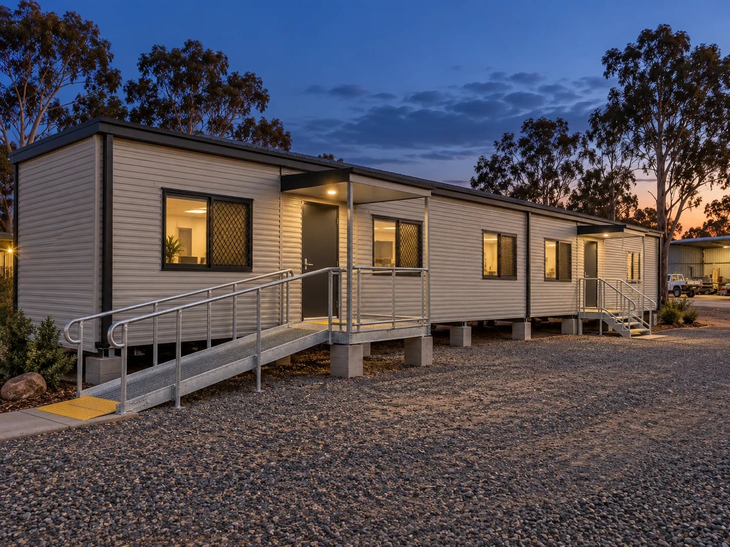 Completed prefab building at dusk with illuminated rooms and entry ramps